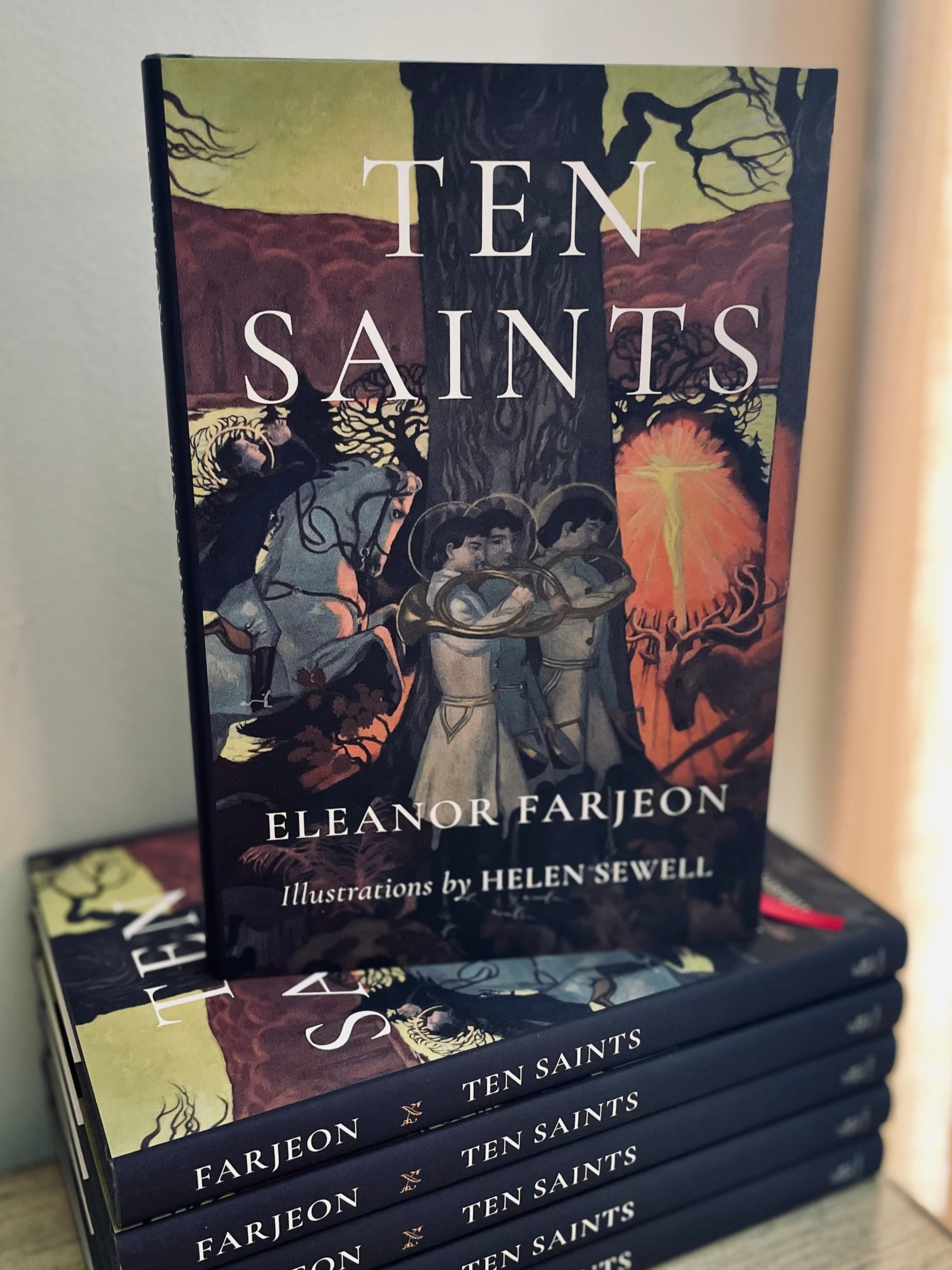 Stack of books titled &#39;Ten Saints&#39; by Eleanor Farjeon with illustrations by Helen Sewell on a wooden surface.